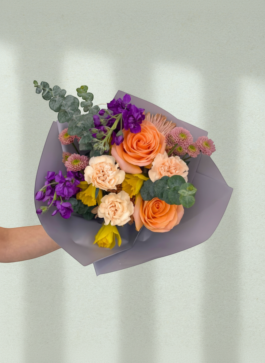 Lakewood Florist bouquet with peach roses, daffodils, carnations, purple stock, and eucalyptus. Vibrant spring arrangement.