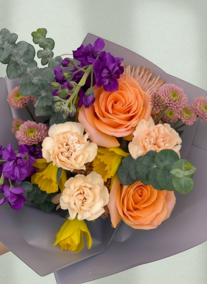 Lakewood Florist bouquet with peach roses, daffodils, purple stock, and pink mums, accented with eucalyptus.