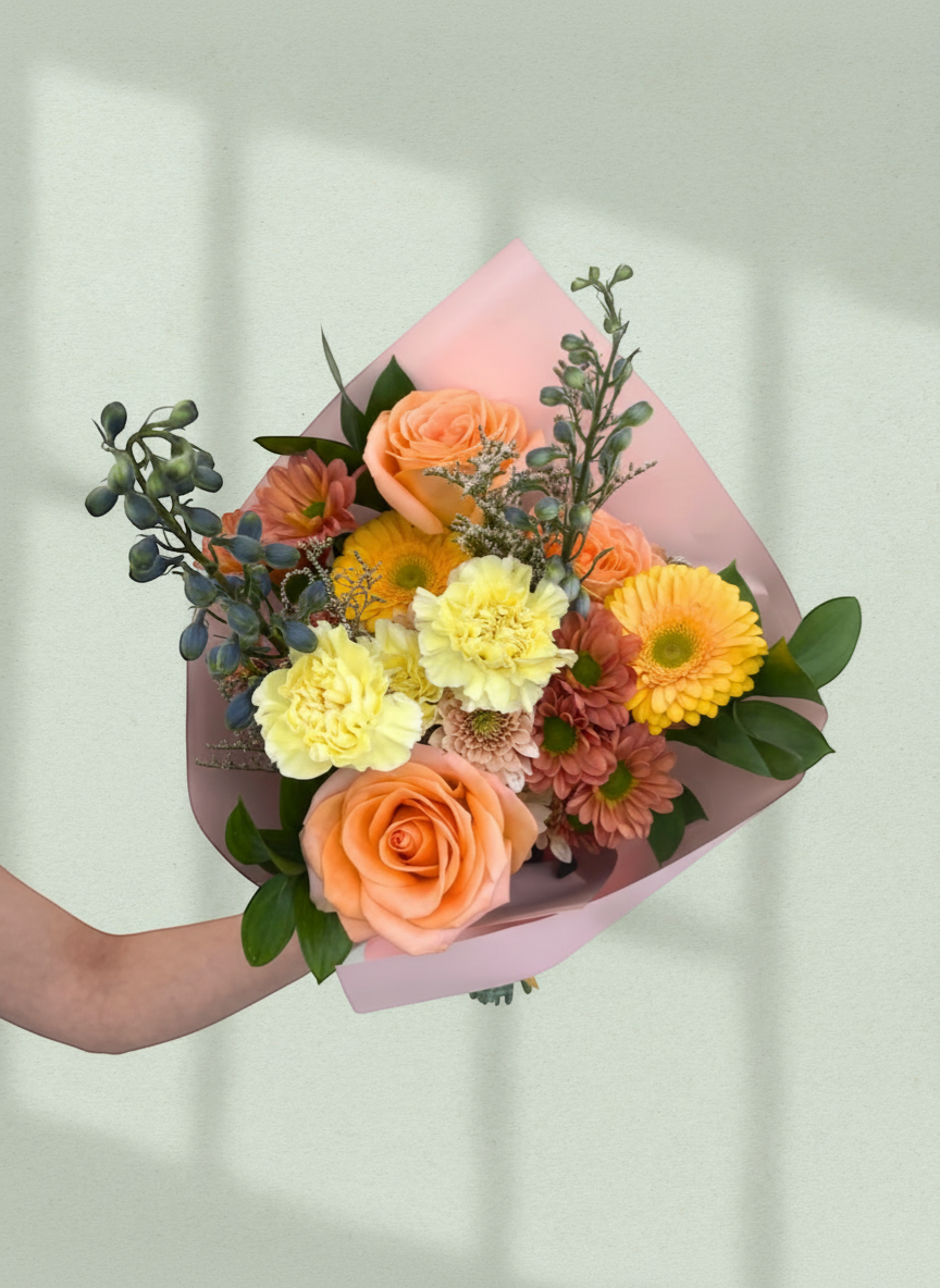 Lakewood Florist bouquet with peach roses, yellow gerbera daisies, carnations, and blue delphinium.